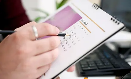 Hand marking a date in a paper calendar planner with a pen