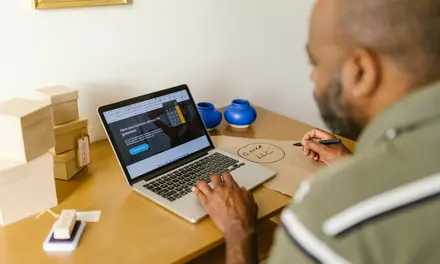 Entrepreneur at a wooden desk working on a laptop with documents and a pen