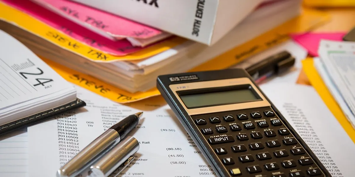 Stack of income tax files with a calculator and two pens