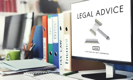 Desk with a monitor showing legal advice and a gavel, beside binders labeled tax, law and finance