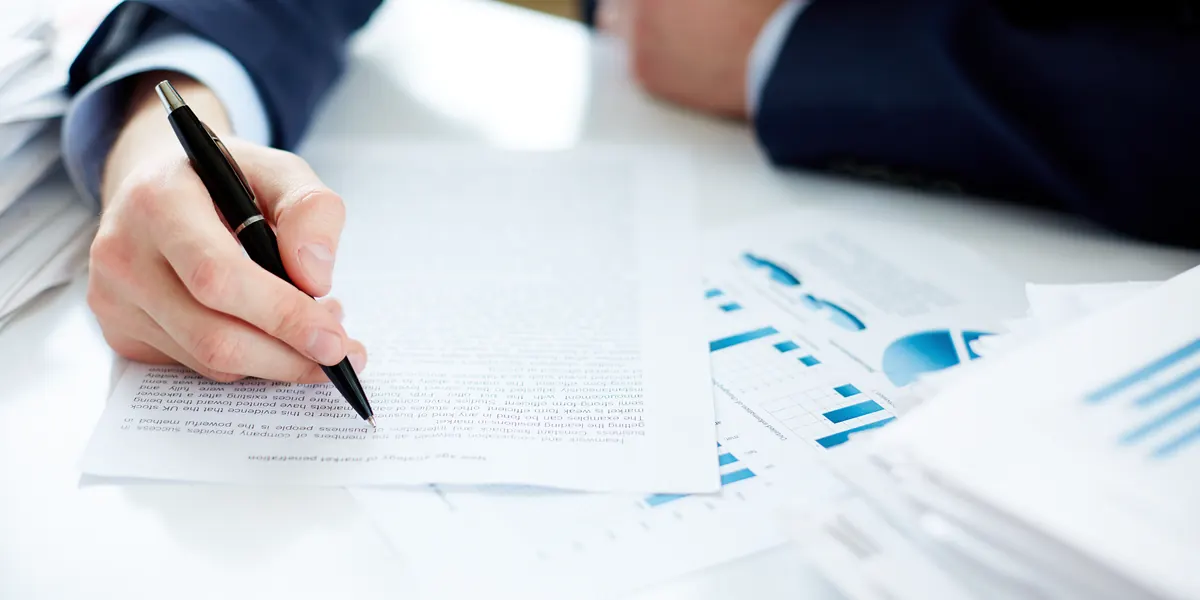 Person signing a report at a desk covered with financial charts
