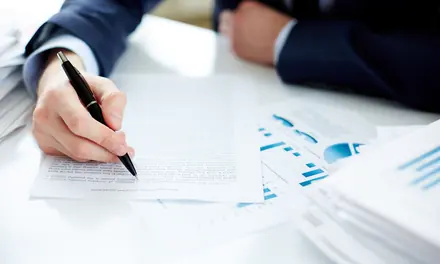 Person signing a report at a desk covered with financial charts