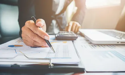 Hand pointing with a pen at financial charts on a desk