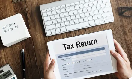 Hands holding a tablet showing a tax return form on a desk with a keyboard