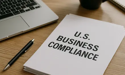 Folder labeled U.S. Business Compliance on a desk with a laptop, a pen and a coffee mug